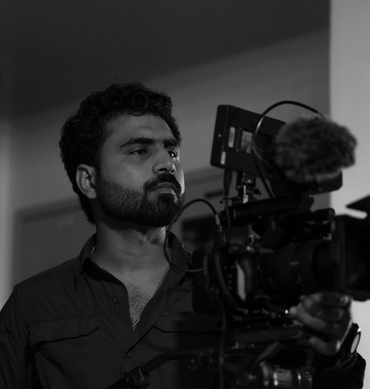 Black-and-white behind-the-scenes portrait of Bilal Ismat operating a cinema camera.